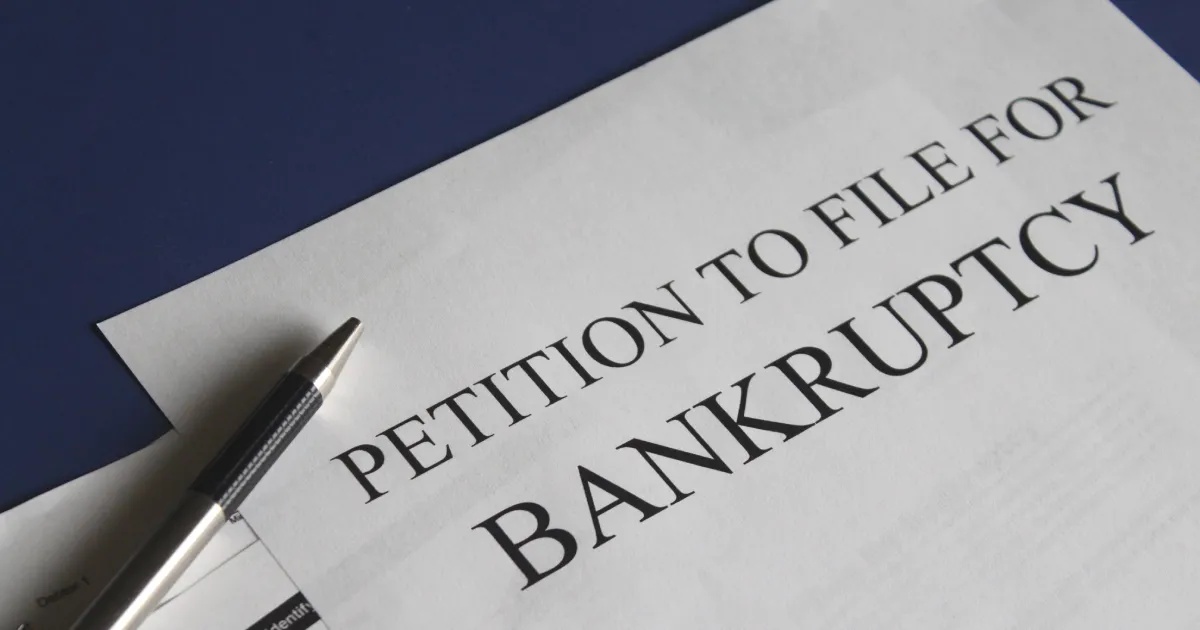 A "Petition to File for Bankruptcy" document with a pen on a dark surface.