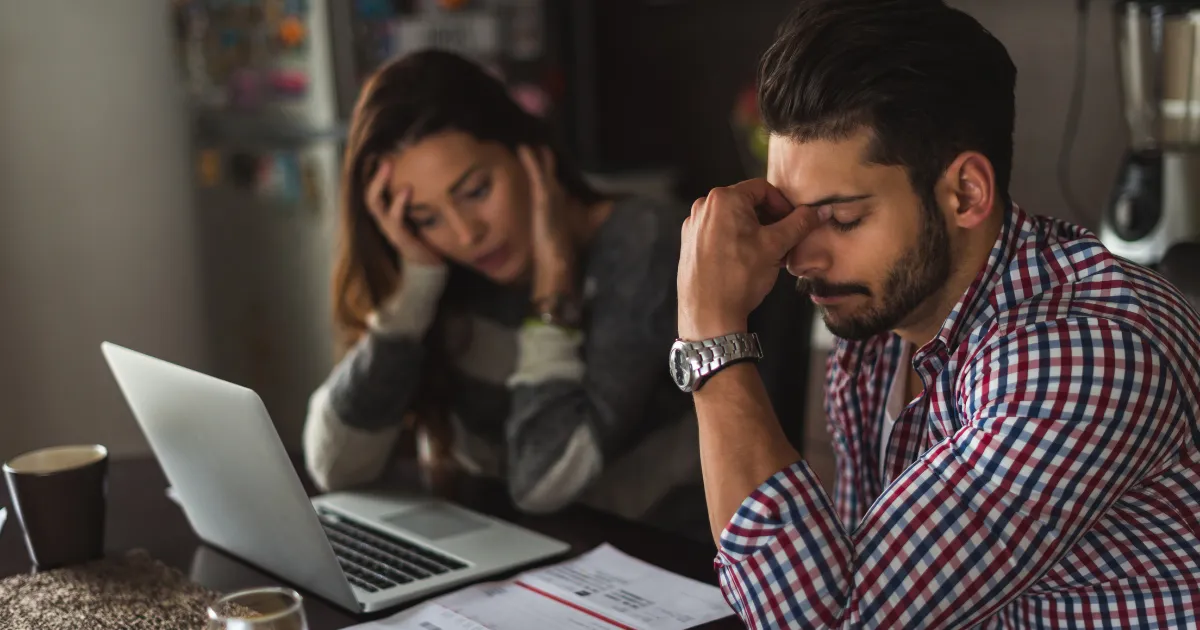 A stressed couple looking overwhelmed while sitting at a table with a laptop.