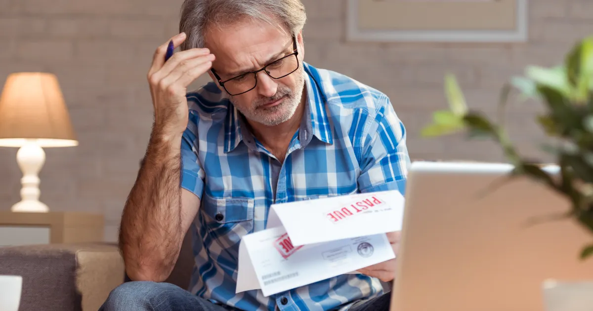 A stressed man looking at past-due bills at a desk.