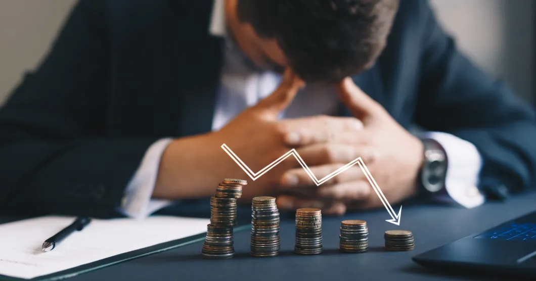 A stressed man sitting behind a declining chart of stacked coins.