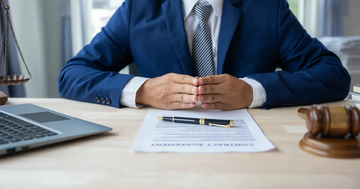 A lawyer or attorney sitting at a desk with a contract, gavel, and scales of justice.