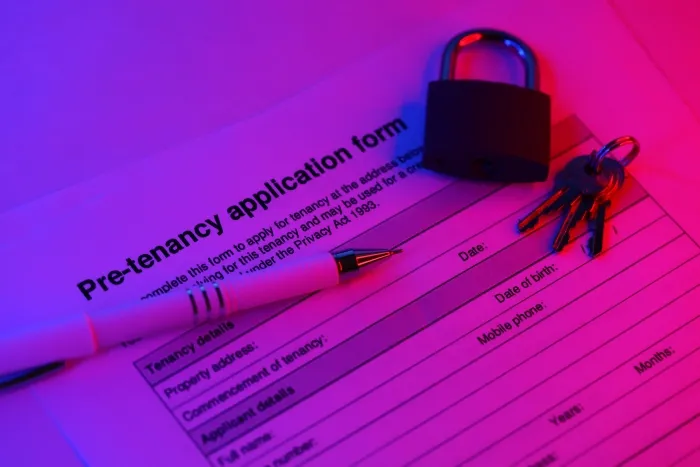 A pre-tenancy application form with a padlock, keys, and a pen under pink and blue lighting.