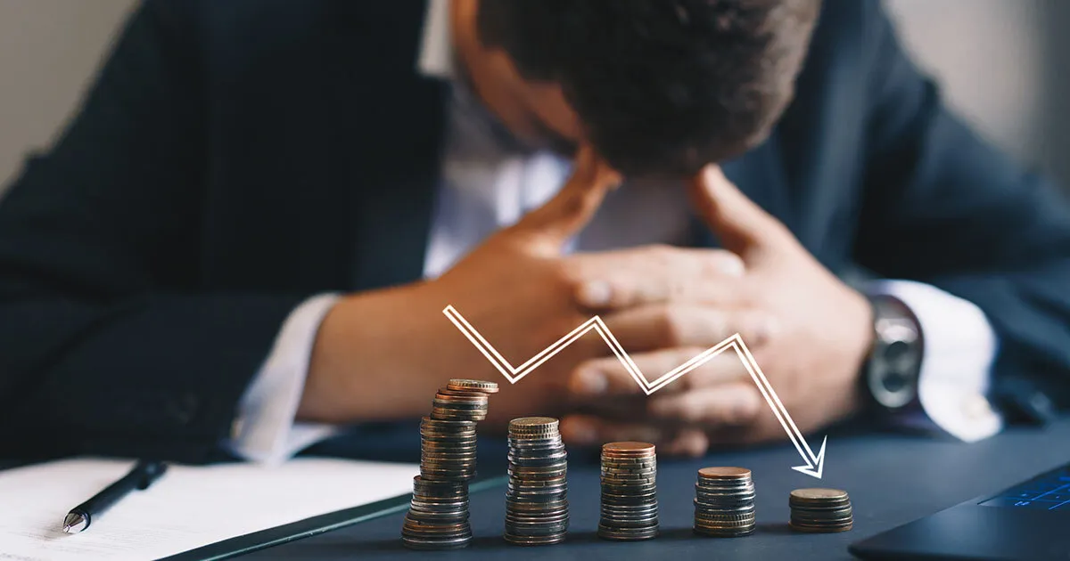 A stressed man sitting behind a declining chart of stacked coins