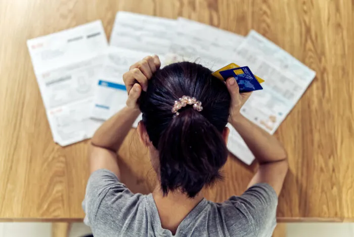 A stressed woman holding her head while looking at bills and credit cards.