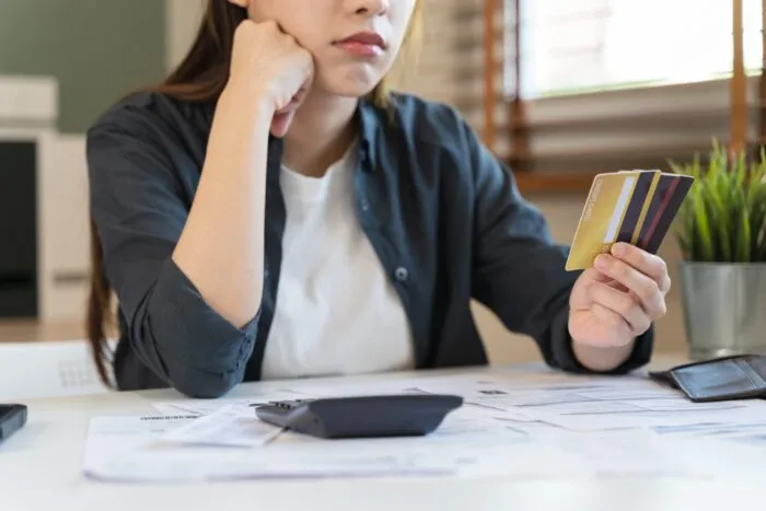 A stressed woman holding credit cards and resting her chin on her hand.